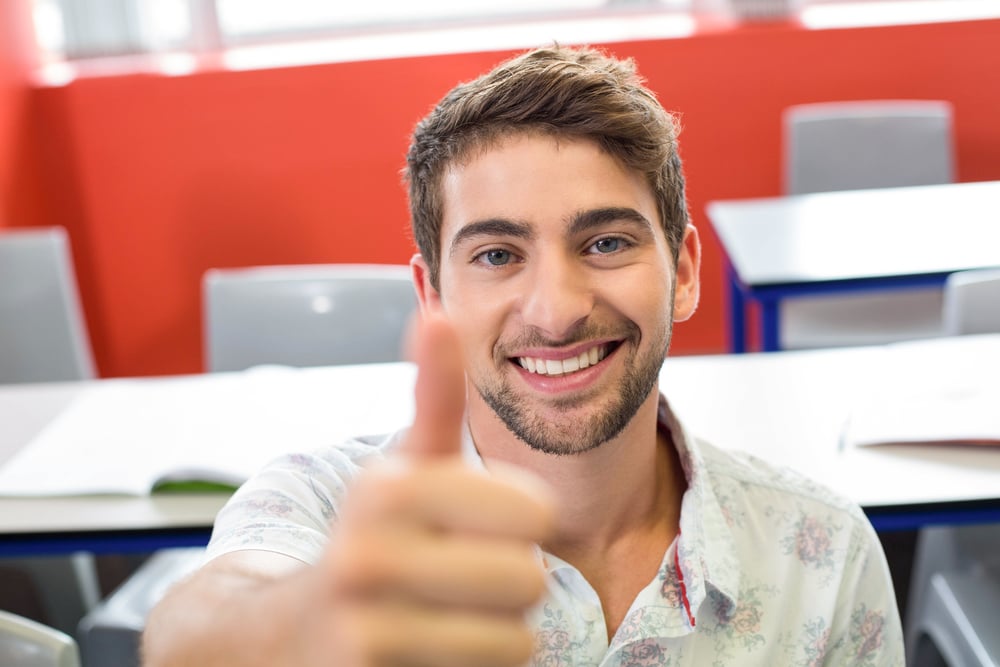 Portrait of smiling male student gesturing thumbs up in classroom