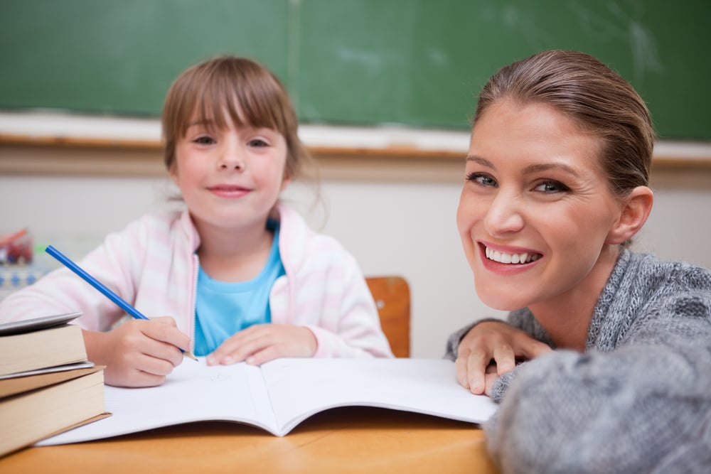 Schoolgirl writing with her teacher in a classroom